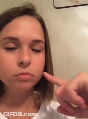A Young Girl With Her Eyes Closed Is Pointing At Her Face GIF