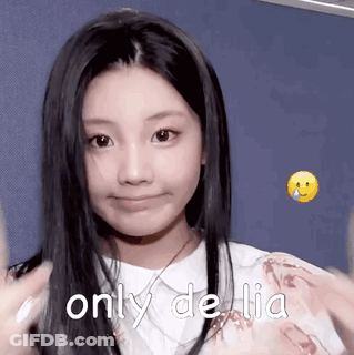 A Young Girl With Long Black Hair Is Smiling And Making A Funny Face While Wearing A White Shirt . GIF