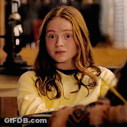 A Young Girl With Long Red Hair Is Wearing A Yellow Sweater And Looking At The Camera . GIF