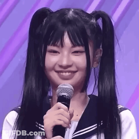 A Young Girl With Pigtails Is Smiling While Holding A Microphone . GIF