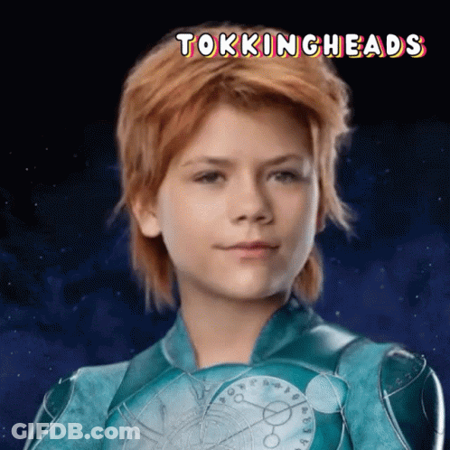 A Young Girl With Red Hair Is Wearing A Blue Superhero Costume With The Words Tokingheads Above Her GIF