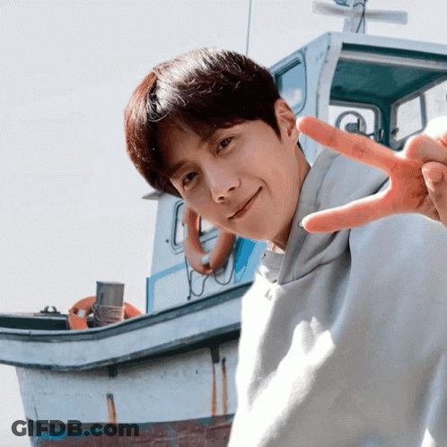 A Young Man Giving A Peace Sign With A Boat In The Background GIF