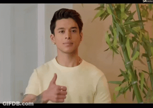 A Young Man Giving A Thumbs Up In Front Of A Bamboo Plant GIF