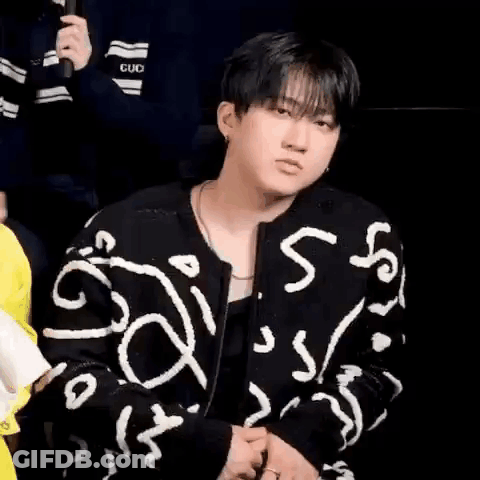 A Young Man In A Black And White Jacket Is Sitting In Front Of A Microphone . GIF