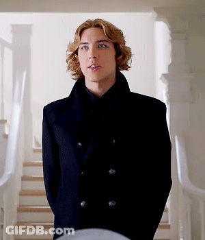 A Young Man In A Black Coat Is Standing In Front Of A Set Of Stairs GIF