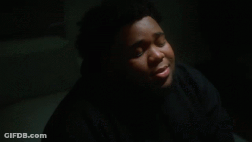 A Young Man In A Black Hoodie Is Sitting In A Dark Room With His Eyes Closed . GIF