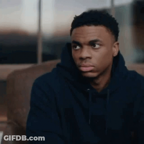 A Young Man In A Black Hoodie Is Sitting On A Couch Looking At Something . GIF