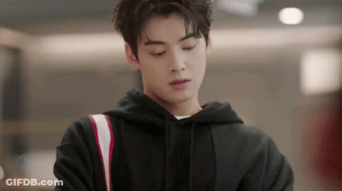 A Young Man In A Black Hoodie Is Standing In A Room Looking Down . GIF
