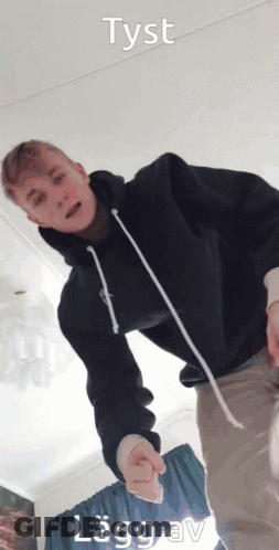 A Young Man In A Black Hoodie Is Standing In A Room With The Words Tyst Lagg Av Written Above Him GIF