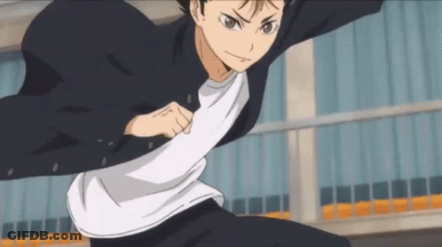 A Young Man In A Black Jacket And White Shirt Is Standing In Front Of A Building In A Karate Pose . GIF