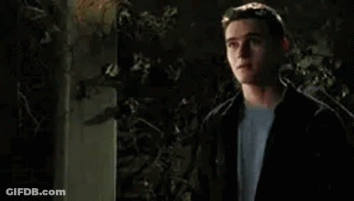 A Young Man In A Black Jacket And White Shirt Is Standing In Front Of A Tree At Night . GIF