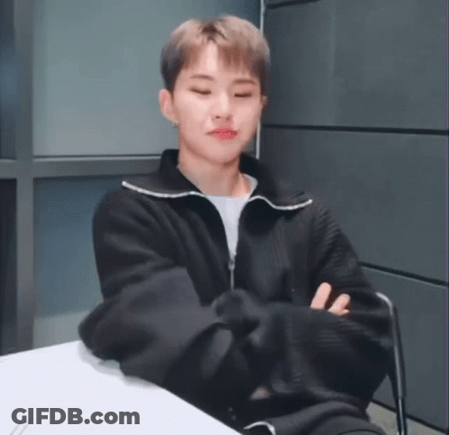 A Young Man In A Black Jacket Is Sitting At A Table With His Arms Crossed And His Eyes Closed . GIF