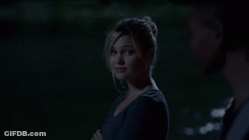 A Young Man In A Black Shirt And Gray Vest Is Standing In The Dark . GIF