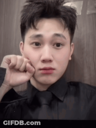 A Young Man In A Black Shirt And Tie Is Taking A Selfie With His Hand To His Face . GIF