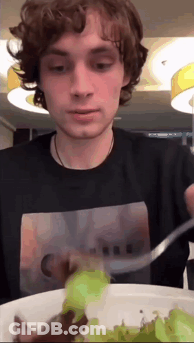 A Young Man In A Black Shirt Is Eating A Salad GIF