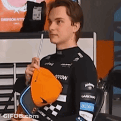 A Young Man In A Black Shirt Is Holding An Orange Hat In His Hands . GIF