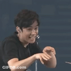 A Young Man In A Black Shirt Is Making A Funny Face With His Hand . GIF