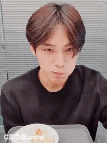 A Young Man In A Black Shirt Is Sitting At A Table With A Bowl Of Food . GIF