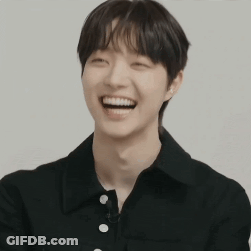 A Young Man In A Black Shirt Is Smiling And Looking At The Camera GIF