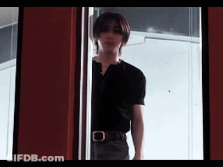 A Young Man In A Black Shirt Is Standing In A Doorway . GIF