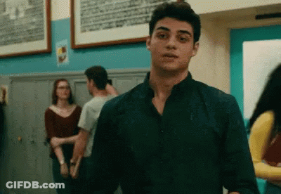A Young Man In A Black Shirt Is Standing In A Hallway With Other People . GIF
