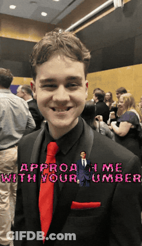A Young Man In A Black Suit And Red Tie Is Smiling With The Words Approach Me With Your Number Behind Him GIF