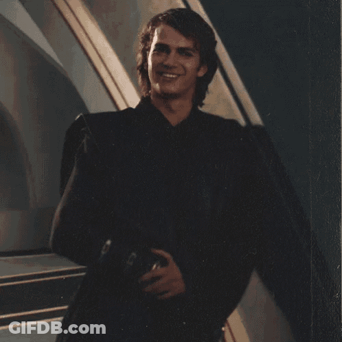 A Young Man In A Black Suit Is Smiling And Holding A Helmet GIF