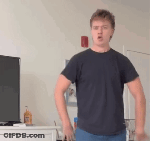 A Young Man In A Black T-Shirt Is Standing In Front Of A Television In A Living Room . GIF