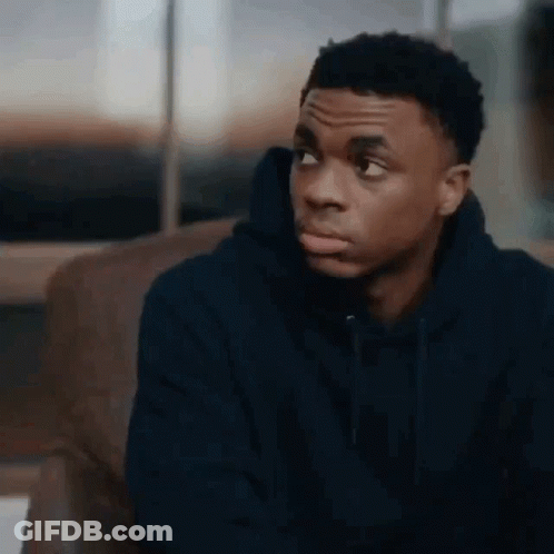 A Young Man In A Blue Hoodie Is Sitting On A Couch And Looking At The Camera . GIF