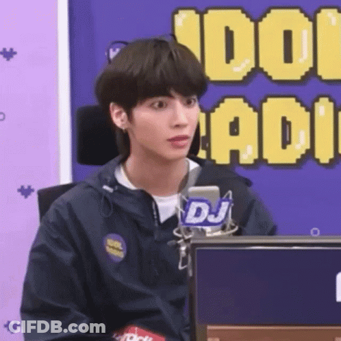 A Young Man In A Blue Jacket Is Sitting In Front Of A Microphone . GIF