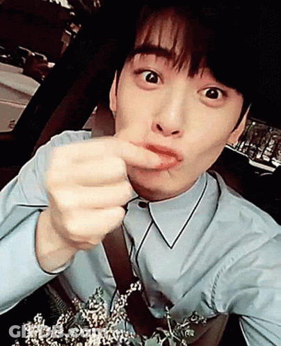 A Young Man In A Blue Shirt Is Holding A Bouquet Of Flowers And Making A Funny Face GIF
