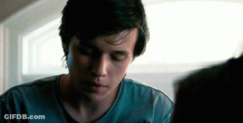 A Young Man In A Blue Shirt Is Looking Down At Something While Sitting In Front Of A Window . GIF