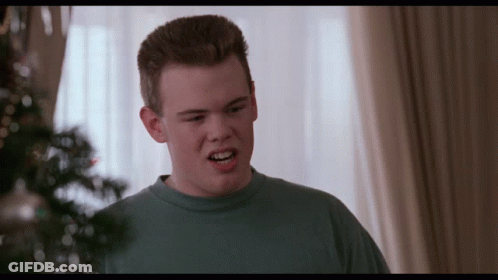 A Young Man In A Blue Shirt Is Making A Face In Front Of A Christmas Tree GIF