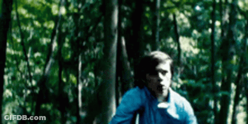A Young Man In A Blue Shirt Is Running Through A Forest . GIF