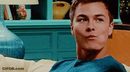 A Young Man In A Blue Shirt Is Sitting On A Couch And Making A Funny Face . GIF