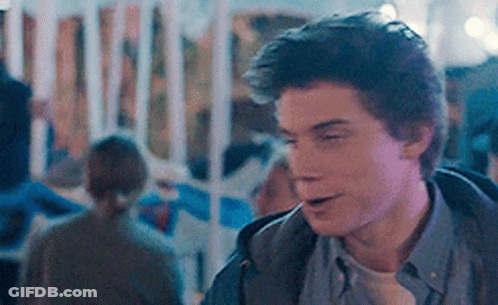 A Young Man In A Blue Shirt Is Standing In A Crowded Area GIF