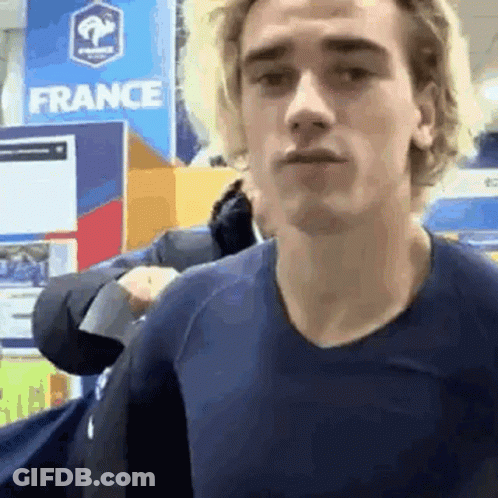 A Young Man In A Blue Shirt Is Standing In Front Of A France Sign . GIF