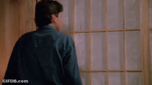 A Young Man In A Blue Shirt Is Standing In Front Of A Window With His Arms Outstretched GIF