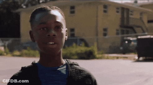 A Young Man In A Blue Shirt Is Standing In Front Of A Yellow Building GIF