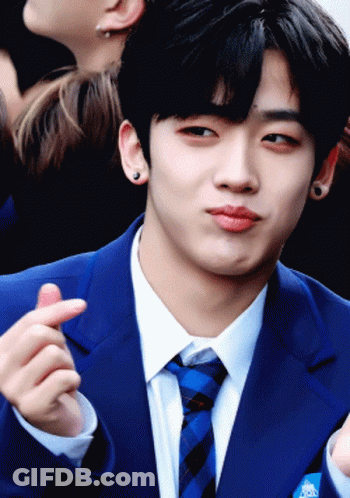 A Young Man In A Blue Suit And Tie Is Making A Heart Shape With His Finger GIF