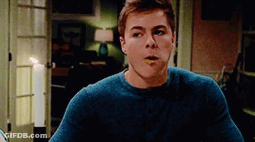 A Young Man In A Blue Sweater Is Eating Something With His Mouth Open GIF
