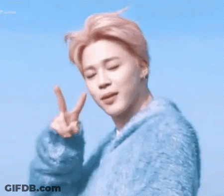 A Young Man In A Blue Sweater Is Making A Peace Sign GIF