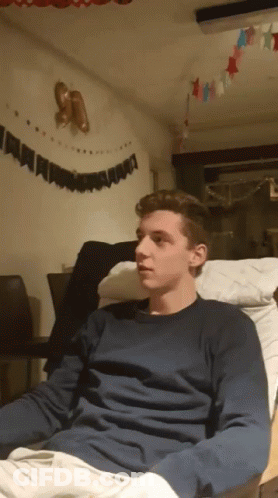 A Young Man In A Blue Sweater Sits On A Chair GIF