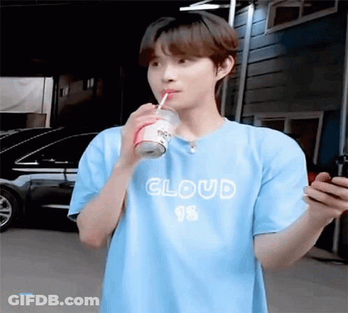 A Young Man In A Blue T-Shirt Is Drinking A Soda Through A Straw While Looking At His Phone . GIF
