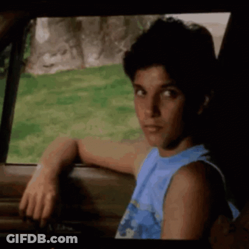 A Young Man In A Blue Tank Top Is Leaning On The Door Of A Car . GIF
