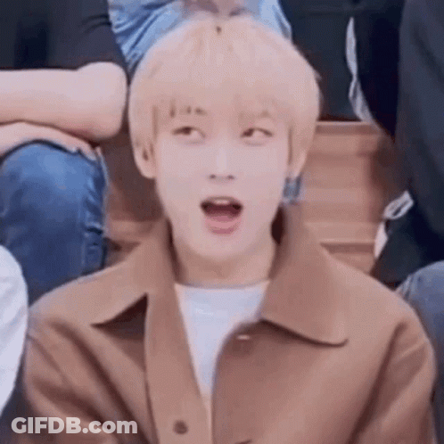 A Young Man In A Brown Jacket Is Sitting In A Crowd With His Mouth Open . GIF