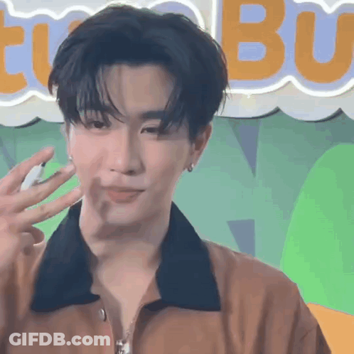 A Young Man In A Brown Jacket Is Waving His Hand In Front Of A Neon Sign . GIF