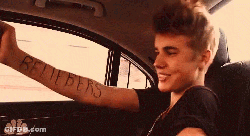 A Young Man In A Car With A Tattoo On His Arm That Says Beliebers GIF