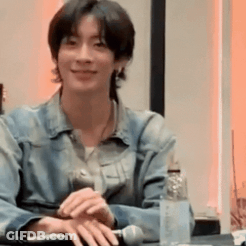 Young Man In Denim Jacket Smiling At Table GIF