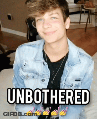 A Young Man In A Denim Jacket Is Sitting On A Couch With The Words " Unbothered " Below Him GIF